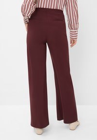 Pantaloni a gamba larga bordeaux con vita alta e due tasche posteriori, realizzati in un tessuto morbido, abbinati a una camicia a maniche lunghe a righe.