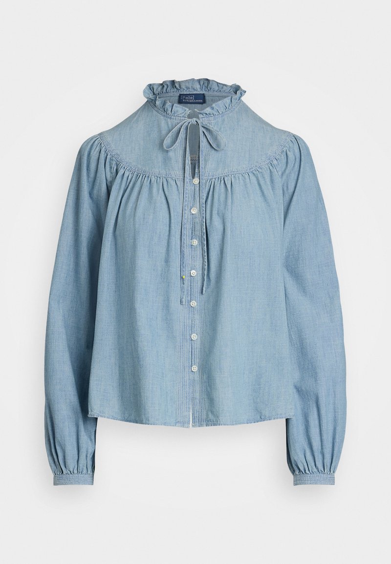 Blouse en denim bleu clair avec un col ruffle haut et un nœud à l'avant. Présente des manches longues légèrement bouffantes et une fermeture à boutons sur le devant.