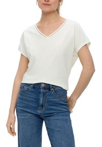Biała koszulka z dekoltem w serek, z fakturowanym wykończeniem, krótkimi rękawami i luźnym krojem, zestawiona z niebieskimi dżinsami o wysokim stanie.