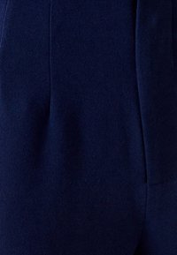 Marinblå tyg med en mjuk, borstad textur; skräddarsydd design med subtila veck och en sidoficka för ökad funktionalitet.