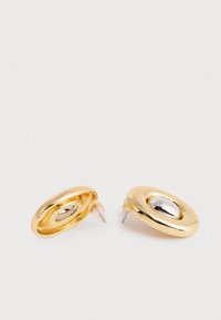 Kuld- ja hõbedatooni ovaalsed studs-kõrvakad tühja keskosaga, plastik- ja metallitoega, valge tausta peal.