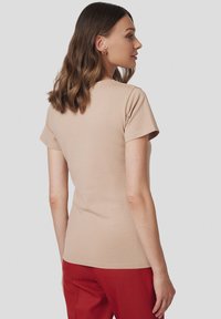 Beżowa dopasowana koszulka z krótkim rękawem, gładka w dotyku, z okrągłym dekoltem i minimalistycznym wzorem, zestawiona z czerwonymi spodniami.