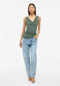Haut sans manches drapé vert avec des détails froncés, associé à un jean bleu clair ample et des sandales à brides. Design et textures simples.