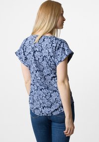 Top floreale blu navy con maniche corte a cappuccio, caratterizzato da una texture morbida e un orlo curvo. La vista posteriore mostra una vestibilità complessiva rilassata.