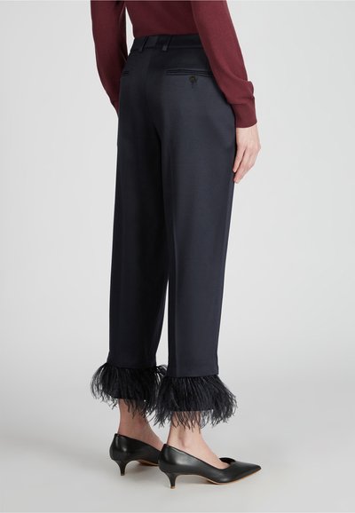Pantaloni blu navy a gamba larga, con dettagli in piuma all'orlo e tasche posteriori. Indossati con décolleté nere a punta.