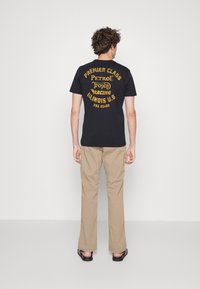 Schwarzes Baumwoll-T-Shirt mit gelbem Grafiktext auf dem Rücken, der "PREMIER CLASS PETROL Trophy RACING ILLINOIS U.S. USA 60433" lautet.