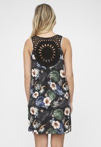 Sort hækledekoration på en blomstermønstret kjole med flerfarvede blade og blomster på en mørk baggrund. Ærmeløs design.