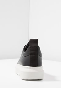 Baskets en cuir noir à finition lisse, avec languette arrière élastique et semelle en caoutchouc blanche. Design minimaliste avec détails de couture discrets.