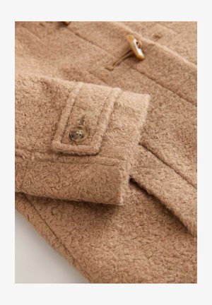 Smėlio spalvos vilnos paltas su faktūruotu paviršiumi, turintis mygtukų užsegimą ir kišenę su atvartu, pabrėžiantis minkštą, pūkuotą medžiagą.