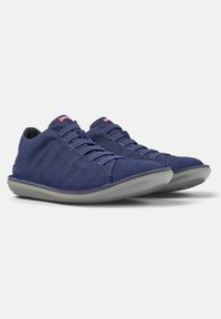 Navy canvas sneakers with gray rubber soles, textured fabric, and lace-up design. Features a brand label on the tongue and subtle stitching details.