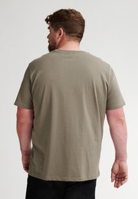 Olivově zelené bavlněné tričko s krátkými rukávy, kulatým výstřihem a volným střih. Hladký povrch a bez viditelných vzorů či log.