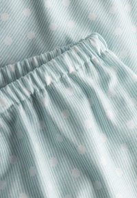Lichtblauwe stof met dunne verticale strepen en verspreide witte stippen. Elastische tailleband met plooien en een gladde textuur.