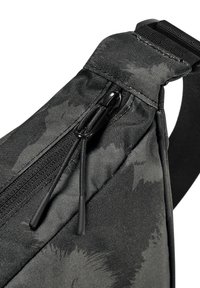 Čierna textilná sling taška s textúrovaným vzorom, ktorá má zipsovú kapsu a elegantné čierne kovanie. Súčasťou je nastaviteľný popruh.