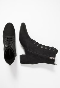 Botas de ante negras hasta el tobillo con puntera puntiaguda, cierre de cordones en la parte delantera, cremallera lateral y tacón grueso. Textura suave con costuras y acentos mínimos.