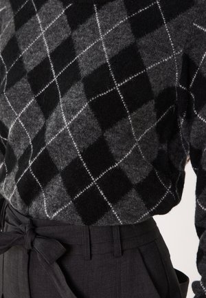 Maglione grigio e nero con motivo argyle, realizzato in tessuto morbido, abbinato a pantaloni neri a vita alta con dettaglio della cintura annodata.