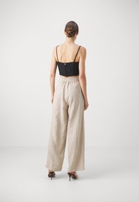 Svart kort topp med spaghetti-brynjor, tillsammans med beiga linnevida byxor med elastisk midja. Klacksandaler fulländar looken.