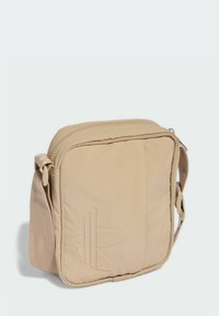 Borsa a tracolla sintetica beige con chiusura a zip, logo in rilievo discreto, tracolla regolabile e texture liscia. Forma quadrata.