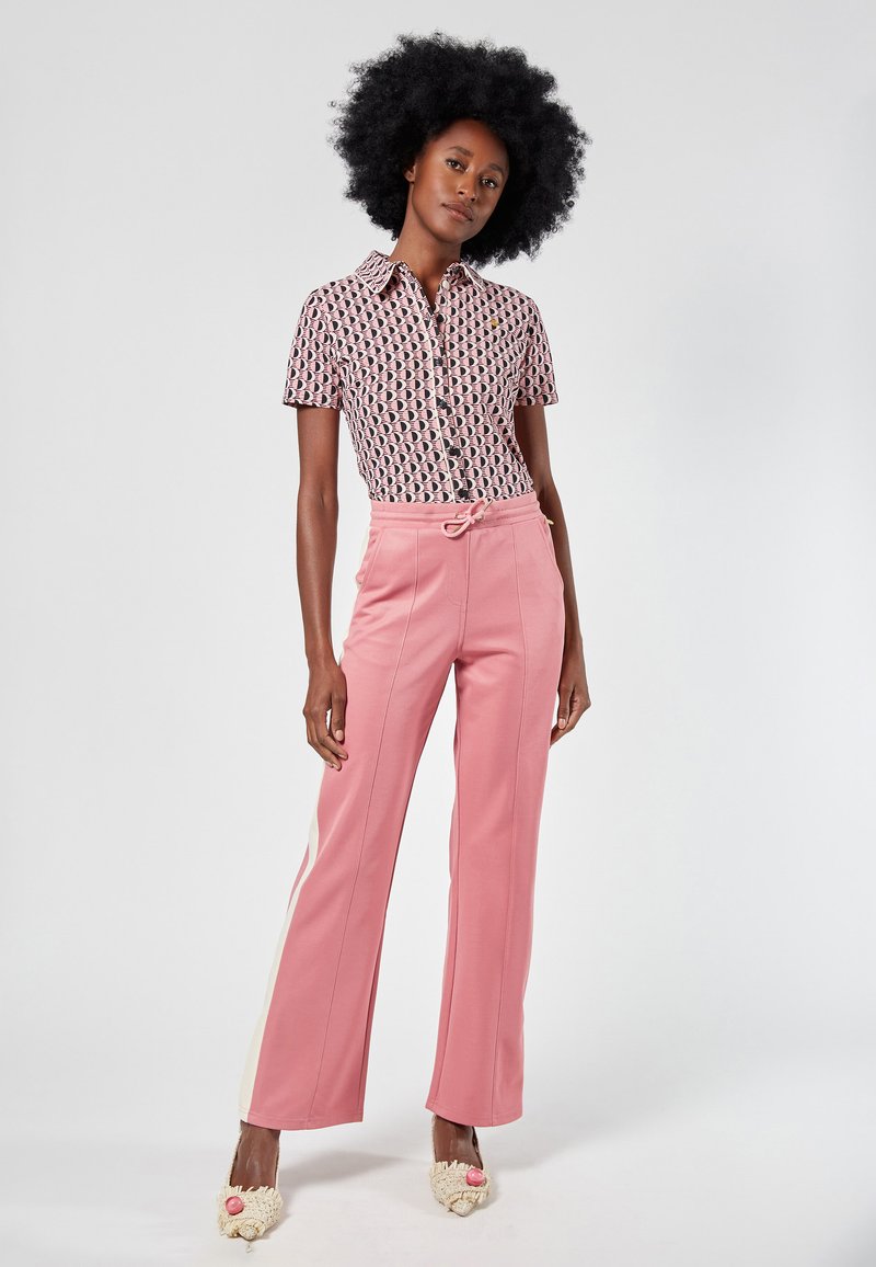 Kurzärmeliges Hemd mit geometrischem Muster in Pink und Marineblau, kombiniert mit hochgeschnittenen rosa Hose mit Seitenstreifen und Kordelzug.