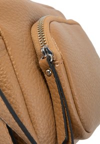 Zoom su una borsa in pelle beige con texture, dotata di una zip in metallo e un tirante in pelle abbinato con bordi neri.