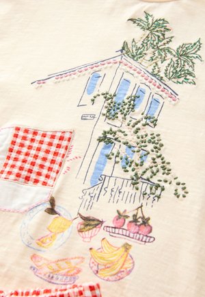 Bestickter Baumwollstoff mit einem Haus, Obst und einer karierten Tasche. Farben umfassen Creme, Blau, Grün, Rot und gelbe Details.