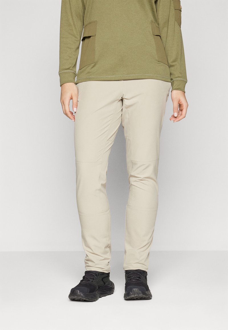 Beige raka byxor i lätt tyg med en lätt lyster. Parar med en grön långärmad topp och svarta sneakers.