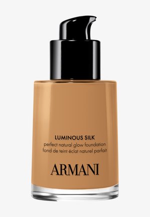 Flacon de fond de teint avec un bouchon pompe. Flacon en verre contenant un liquide beige. Capuchon noir et étiquette avec le texte en gras "Luminous Silk" en noir.