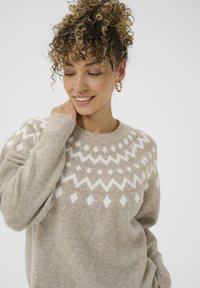 Pulover tricotat bej, cu un model geometric alb, guler rotund și mâneci lungi cu manșete răsucite. Textură moale și o croială lejeră.