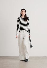Suéter de rayas en blanco y negro combinado con pantalones anchos blancos. La modelo lleva un pequeño bolso negro y calza zapatos negros de punta.