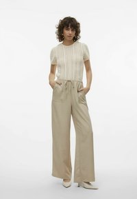 Beige strikbluse med korte ærmer og lodrette mønstre, kombineret med beige bukser med vide ben og sidelommer. Glat tekstur over det hele.