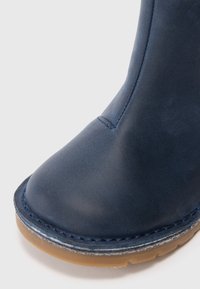 Ναυτικό δερμάτινο μποτάκι στον αστράγαλο με στρογγυλή μύτη, ραμμένο περίγραμμα και καφέ καουτσούκ σόλα. Λείο υλικό με ελαχιστοποιημένες λεπτομέρειες.