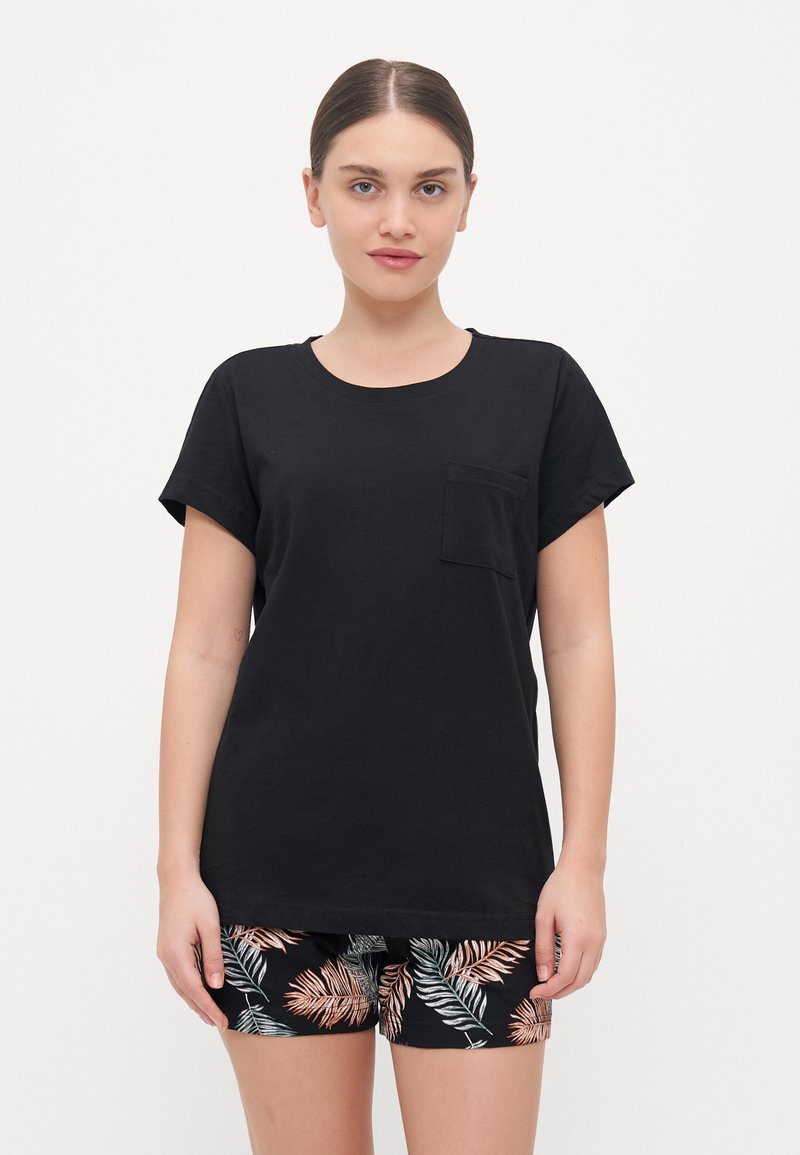 T-shirt de algodão preto com mangas curtas em rolo, decote redondo e um bolso no peito, combinado com calções pretos com um padrão de folhas tropicais.