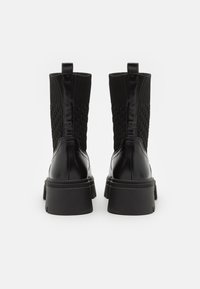 Botine negre până la gleznă, cu un upper din tricot texturat și toc din piele netedă, dotate cu o talpă groasă din cauciuc și un tab pentru a fi ușor de încălțat.