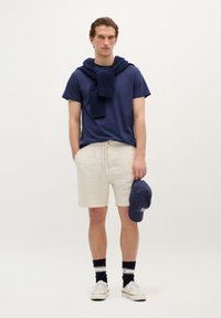 Marineblå t-shirt, beige linned-shorts med snøre, marineblå baseball-cap, hvide sneakers og marineblå stribede sokker. Casual design, afslappet pasform.