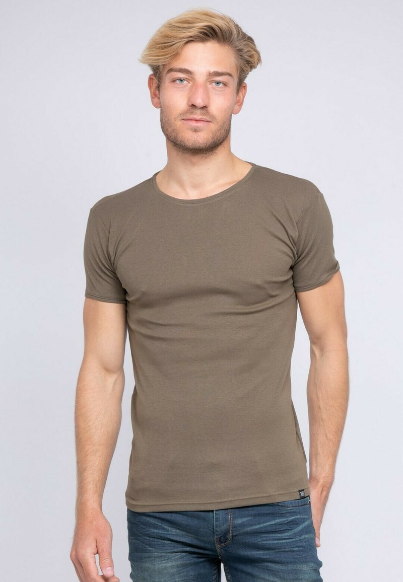 T-shirt à manches courtes de couleur vert khaki en coton doux. Il présente un col rond et une coupe ajustée, porté avec un jean en denim bleu.