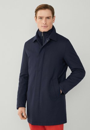 Marineblauwe jas met een kraag, een rits aan de voorkant en zijzakken. Gemaakt van gladde stof met een getailleerde pasvorm.