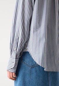 Randig skjorta i blå och vit bomull med långa ärmar, knappmanschetter, rundad nederkant och sidofickor, tillsammans med blå denim.