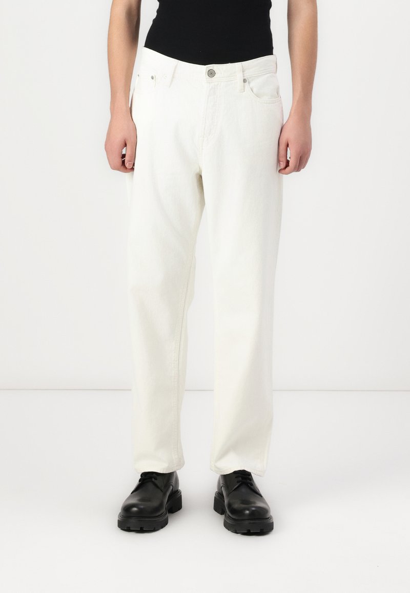 White denim trousers with a loose fit, featuring a button fly, front pockets, and simple stitching, paired with black lace-up shoes.