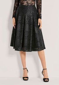 Zwarte kanten rok met geplooid ontwerp, halflang, met ingewikkelde bloemmotieven. Gepaard met zwarte open-teen hakken en enkelbandjes.