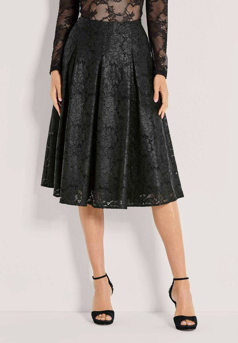 Zwarte kanten rok met geplooid ontwerp, halflang, met ingewikkelde bloemmotieven. Gepaard met zwarte open-teen hakken en enkelbandjes.