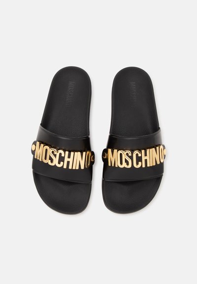 Paire de sandales slides noires avec de larges brides ornées de lettres dorées formant le mot "MOSCHINO" sur chaque bride.