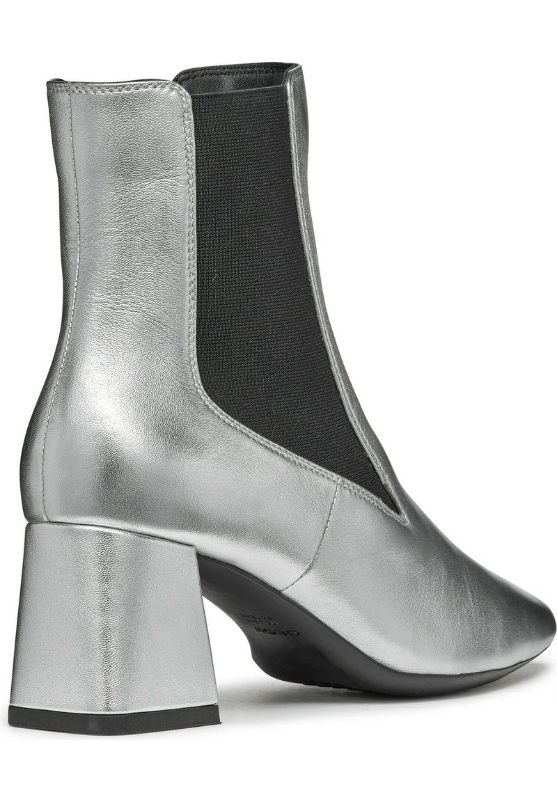 Silberner Knöchelstiefel mit glänzender Metallic-Oberfläche, schwarzen elastischen Seitenpaneelen und einem quadratischen Blockabsatz. Glatte Textur mit leicht spitz zulaufender Zehenpartie.