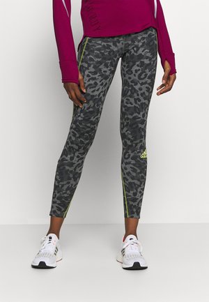 Leggings taille haute en léopard noir et gris avec des bandes latérales vertes, fabriquées en tissu extensible pour flexibilité et confort.