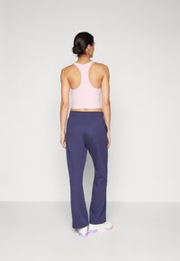 Ružičasti crop top bez rukava, sivi trenirke s elastičnim pojasom i bijele tenisice s ljubičastim detaljima. Glatka tkanina i opušteni kroj.