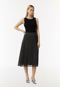 Czarna prążkowana bluzka bez rękawów zestawiona z czarną spódnicą plisowaną z delikatnym wzorem, uzupełniona metalicznymi butami na obcasie.