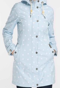 Imperméable à capuche bleu clair avec des pois blancs, fermeture à boutons, poches avant et cordons ajustables avec perles en bois.
