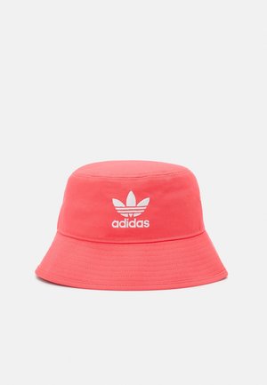 Chapeau bob en tissu rouge avec logo blanc Adidas trefoil centré sur le devant sur un fond gris clair uni.