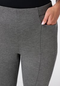 Leggings extensibles gris en tissu texturé, dotés de poches et d'une taille haute pour un ajustement confortable.