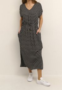 Vestido maxi de patrón en blanco y negro con escote en V, cintura elástica y bolsillos. Combinado con zapatillas blancas, tejido suave y corte relajado.