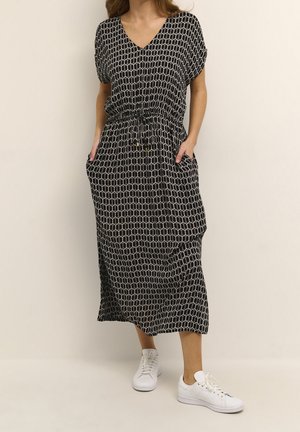 Svart- och vitmönstrad maxiklänning med V-ringning, elastisk midja och fickor. Kombinerad med vita sneakers, mjukt tyg och avslappnad passform.