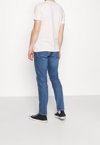 Ljusfärgad t-shirt med rund hals, blå slim-fit jeans, svarta högtoppsneakers, med en enkel design utan synliga mönster eller grafik.